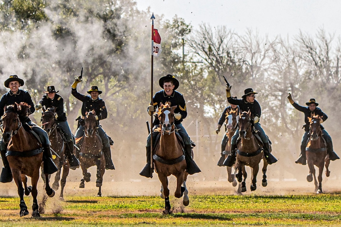 Soldiers wearing cowboy hats ride horses on a field and wave pistols in the air.