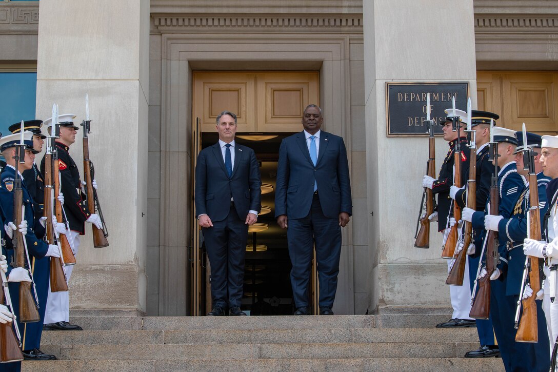 Secretary of Defense Lloyd J. Austin III stands with another civilian on the Pentagon steps, flanked by honor guard troops.