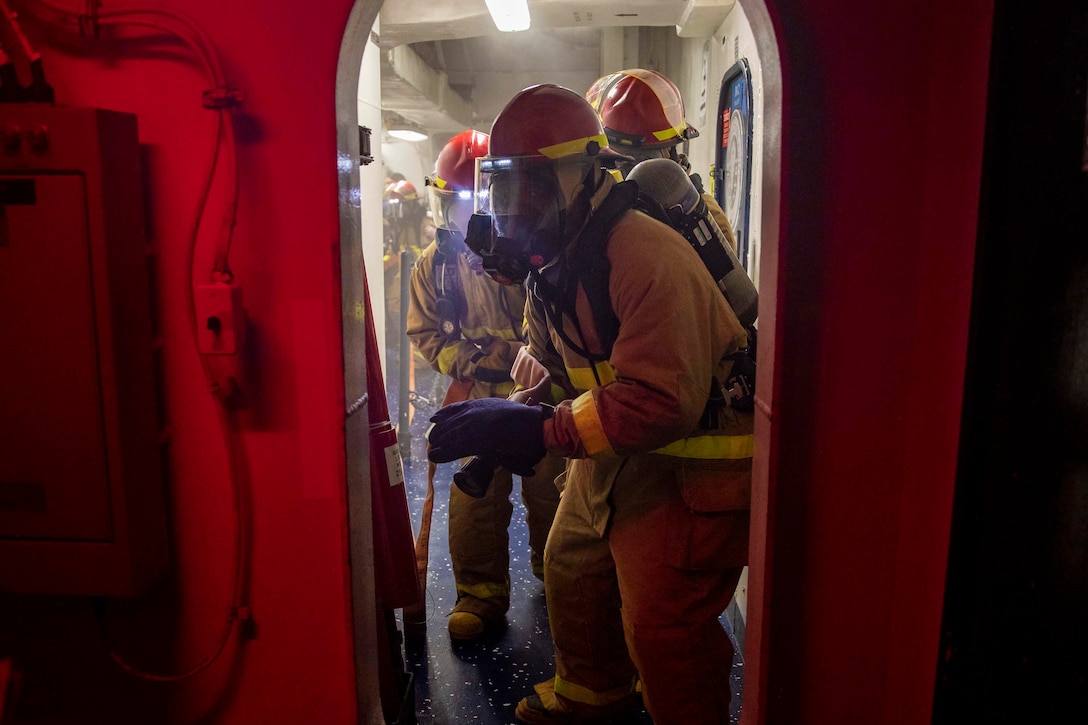 A line of sailors prepare to simulate putting out a fire in quarters aboard a ship.