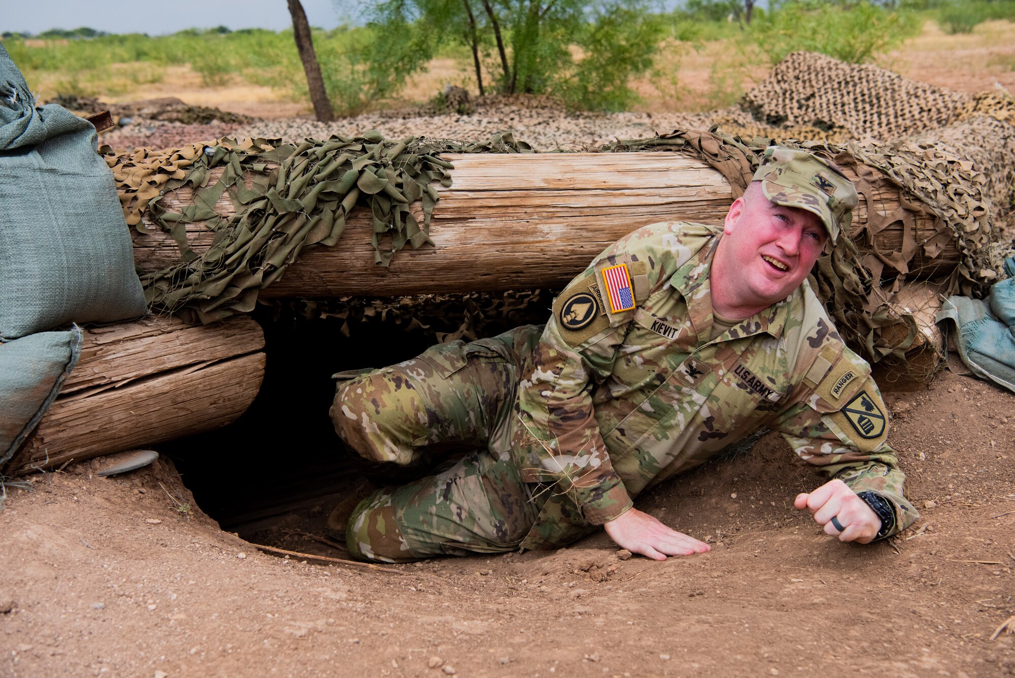 U.S. Army Col. James A. Kievit, Defense Language Institute Foreign Language Center commandant, crawls out of a hidden bunker during a tour of Forward Operating Base Sentinel, at Goodfellow Air Force Base, Texas, July 12, 2022. Students of the 344th Military Intelligence Battalion are tasked to find the source of various signals hidden across FOB Sentinel during their capstone exercise. (U.S. Air Force photo by Senior Airman Michael Bowman)