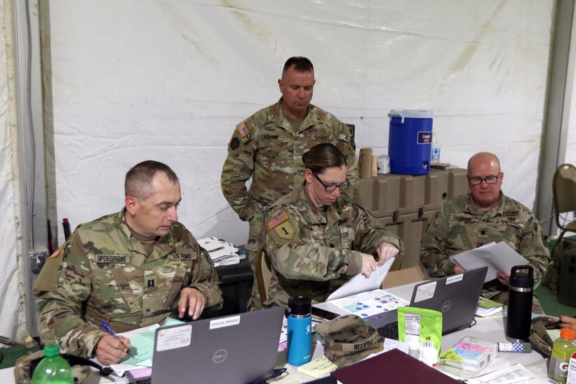 Lt. Col. Andrew O’Connor (right) and Maj. Mike Adams (standing), members of a 28th Infantry Division senior trainer team, review personnel tracking procedures with Capt. Shawn Updegrove (left) and Lt. Col. Alicia Partin, both with the 213th Regional Support Group, June 21, 2022 at the National Training Center, Fort Irwin, Calif. Partin and Updgrove served as the mayor and assistant mayor, respectively, of the 213th’s white cell established at Fort Irwin in support of the 56th Stryker Brigade Combat Team’s NTC rotation.