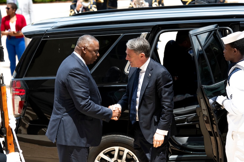 Two men shake hands next to a car.