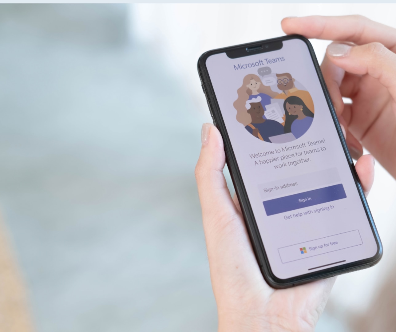 Hand holding mobile phone, screen showing Microsoft Teams application login