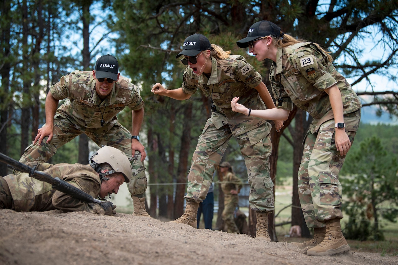 Three instructors yell at a cadet on the ground.