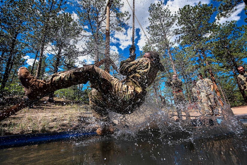 A cadet swings on a rope over muddy water.