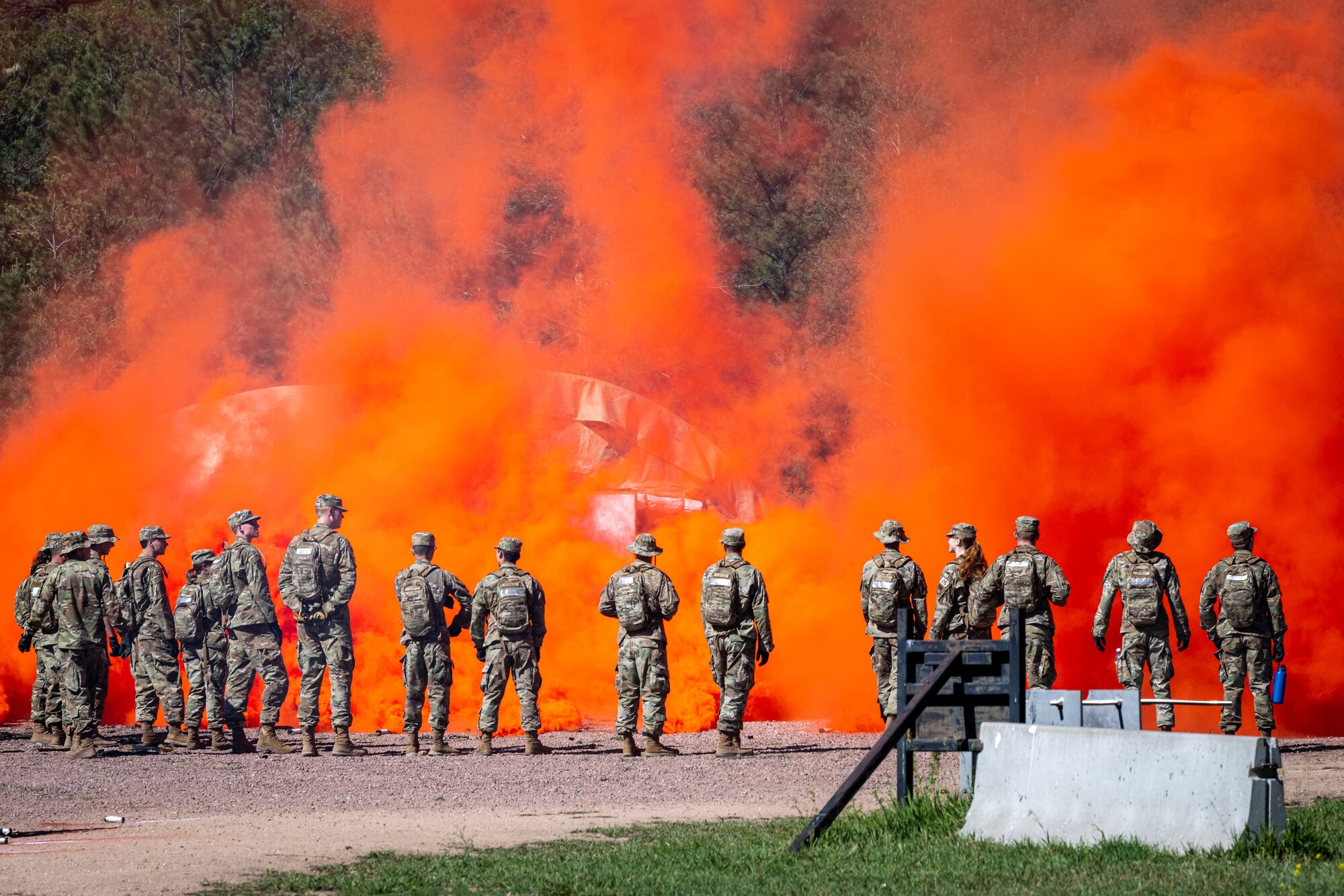 Cadets and cadre members stand near orange flare smoke during combat survival training