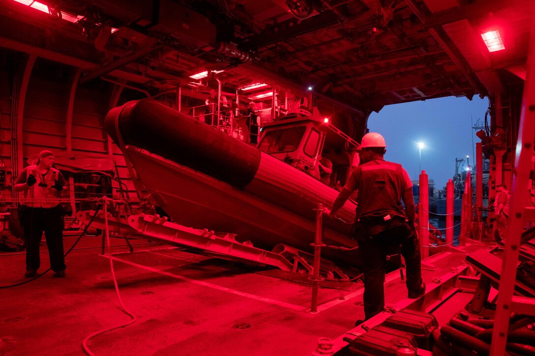 Sailors train in a small inflatable boat in a room with red lights.