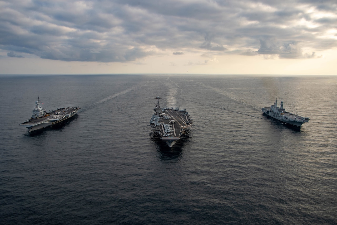 Three large military ships move through the sea.