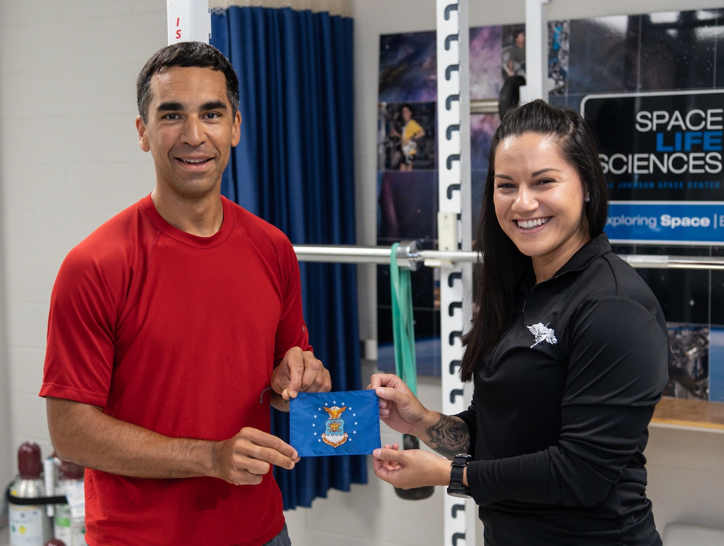 U.S. Air Force Staff Sgt. Emily Valdovinos (right), Special Warfare Human Performance Squadron physical medicine technician, poses for a portrait with Col. Raja Chari (left), NASA astronaut, with a USAF flag that Chari brought aboard the International Space Station at the Johnson Space Center in Houston, Texas, Jun. 16, 2022. Valdovinos was hand-selected by the NASA Astronaut Strength, Conditioning and Rehab Group to help develop personalized strength, conditioning, mobility, and rehabilitative plans for NASA astronauts.