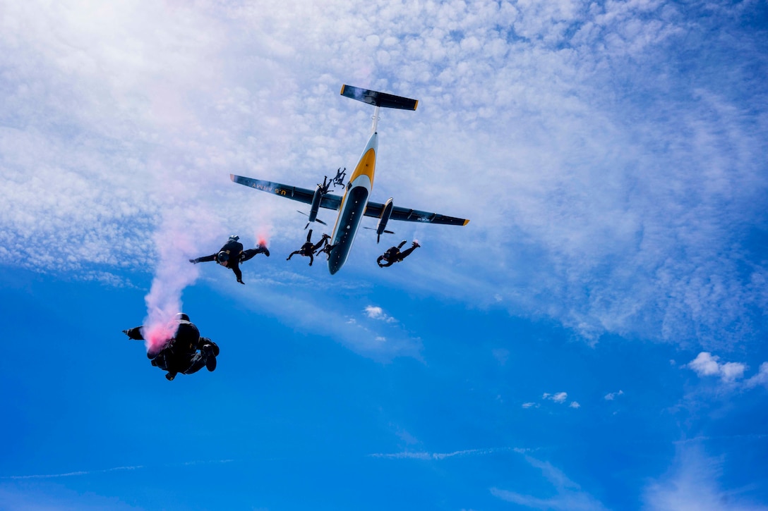 Soldiers jump from an airborne aircraft.