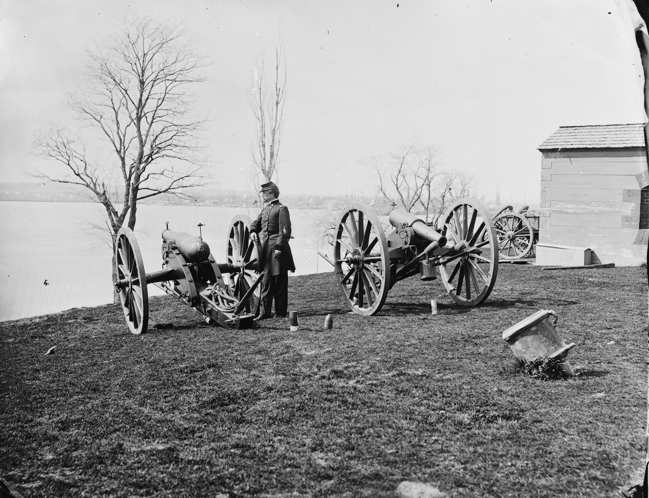 A man stands beside one of two large-caliber guns on wheels.