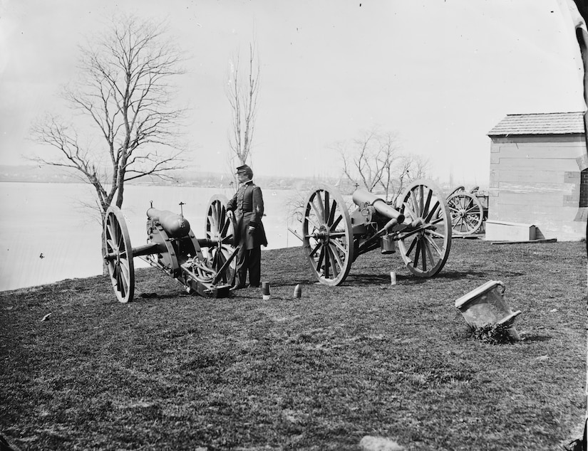 A man stands beside one of two large-caliber guns on wheels.