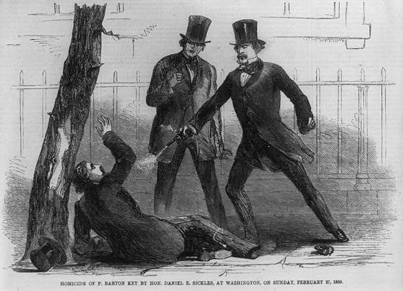 A man shoots a man lying on the ground as a third man watches.