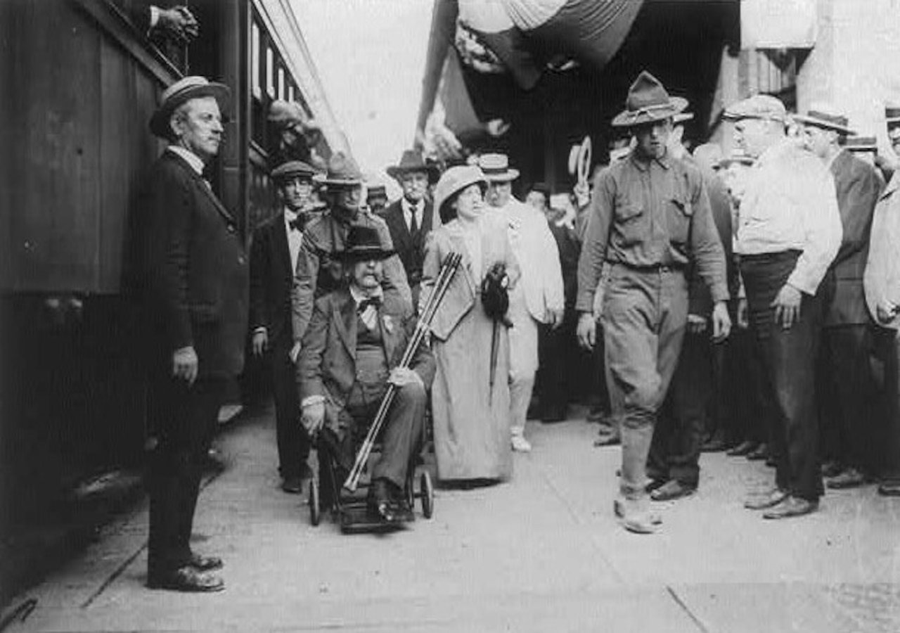 A man in a wheelchair and several others move along a train platform.