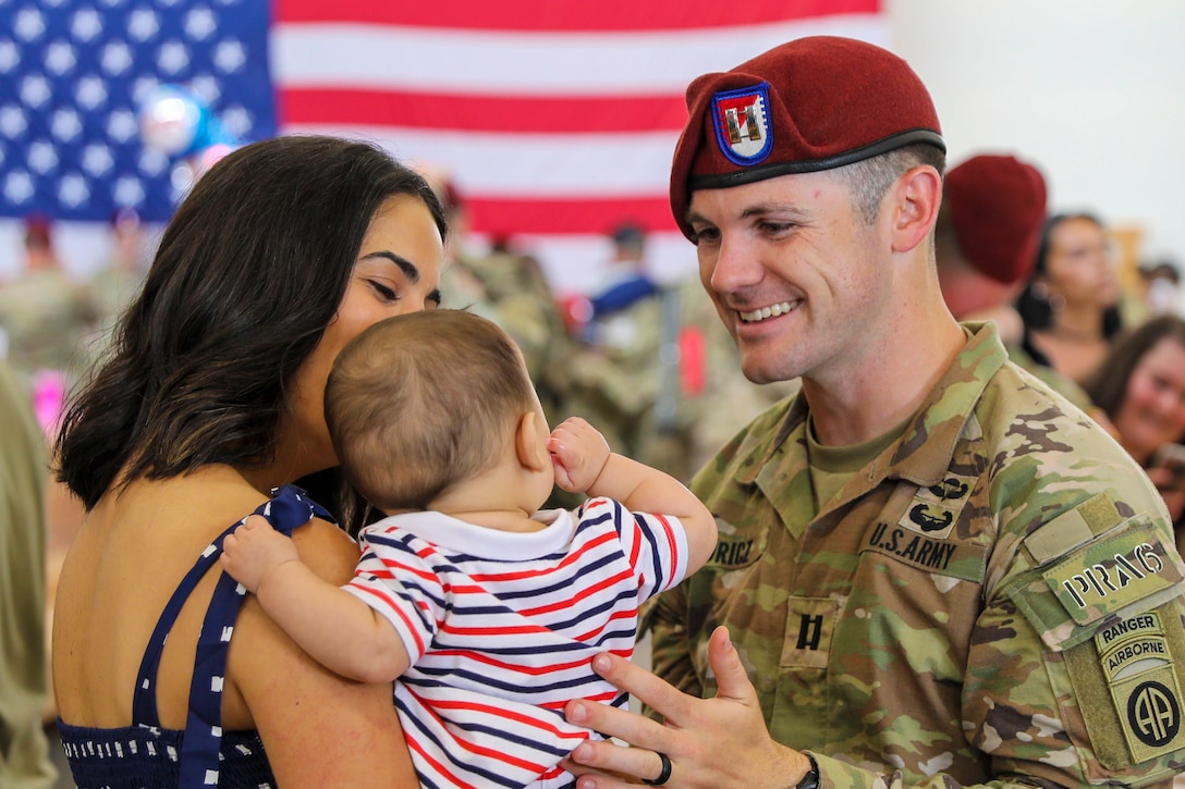 A soldier smiles at a woman holding a baby.