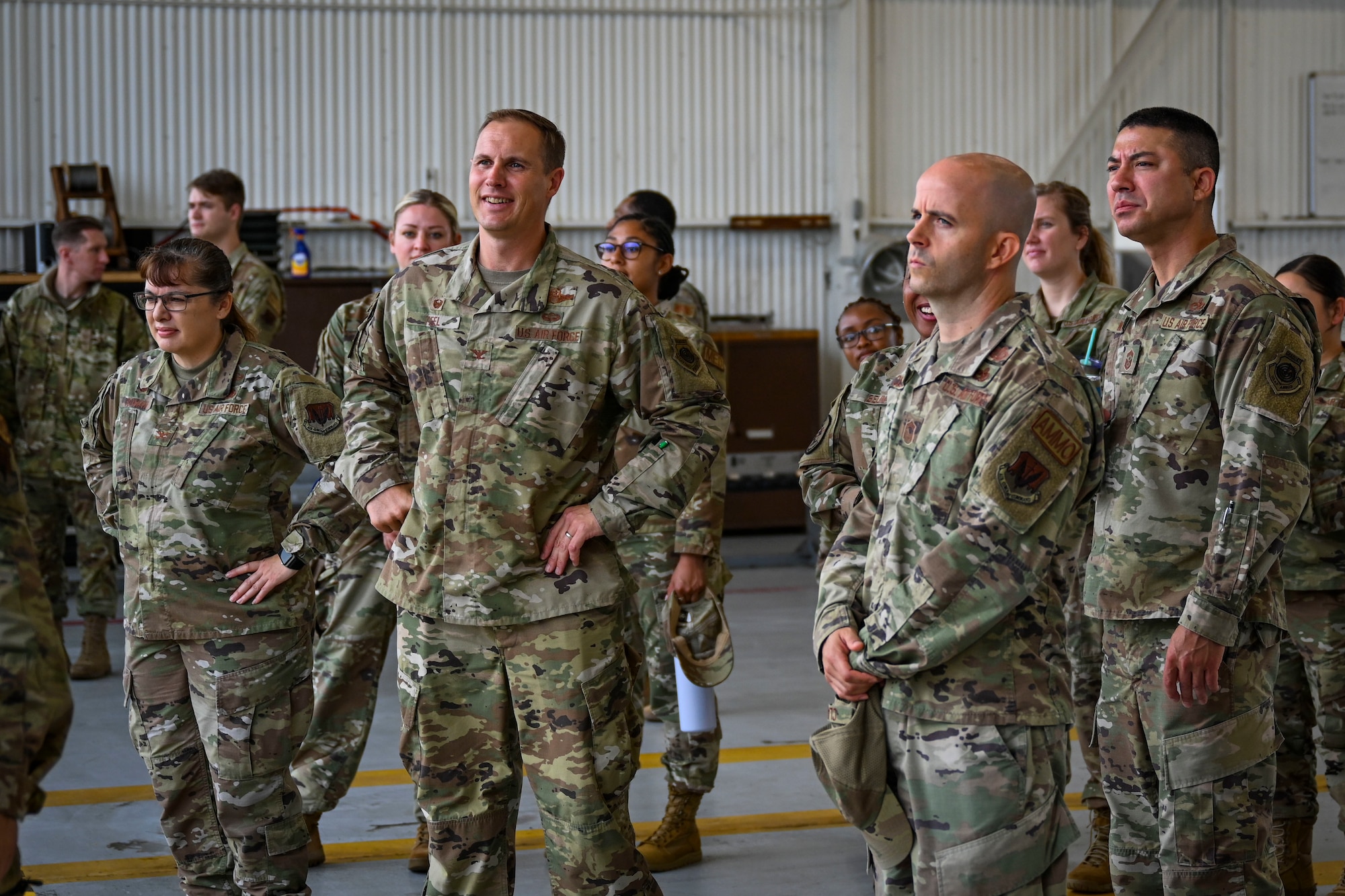 Col. Lucas Teel, center, 4th Fighter Wing commander, and 4th FW Airmen watch a quarterly load crew competition at Seymour Johnson Air Force Base, North Carolina, July 15, 2022. Participants of the competition were judged on their accuracy, serviceability, and efficiency of loading weapons onto an F-15E Strike Eagle. (U.S. Air Force photo by Senior Airman David Lynn)