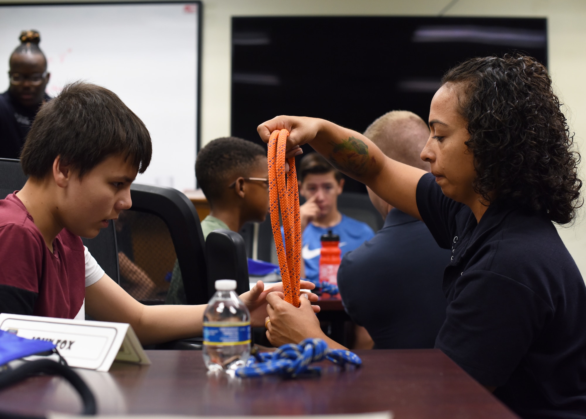 Crystal Casas, 17th Civil Engineer Squadron firefighter driver operator, shows John Fox, junior firefighter camp student, how to tie a knot at Goodfellow Air Force Base, Texas, July 13, 2022. Students learned various knots and hitches that have common uses in firefighting. (U.S. Air Force photo by Airman 1st Class Zachary Heimbuch)