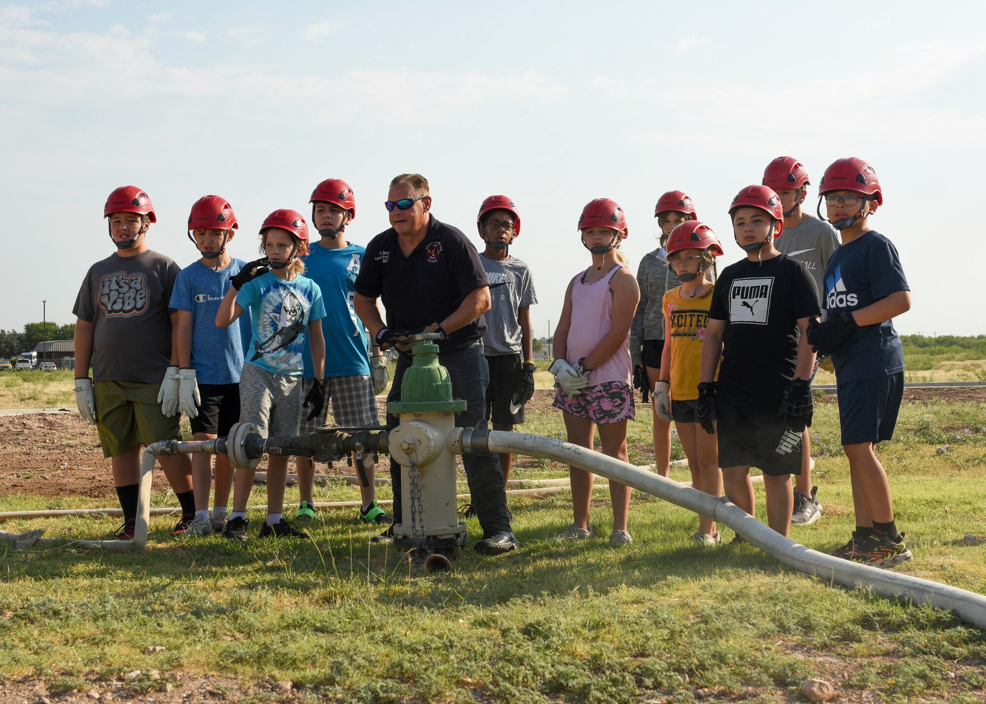 Junior firefighter camp students watch as a fire hydrant is opened to supply water to a fire truck, at Goodfellow Air Force Base, Texas, July 14, 2022. There were 12 junior firefighters who participated in the week-long camp. (U.S. Air Force photo by Airman 1st Class Zachary Heimbuch)