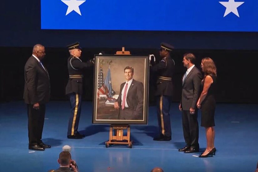 Five people on a stage watch as a portrait is unveiled.