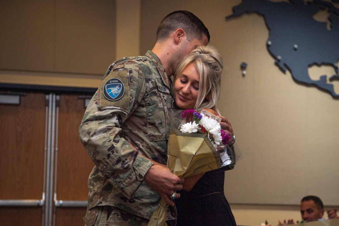 Man in military uniform hugs woman with flowers