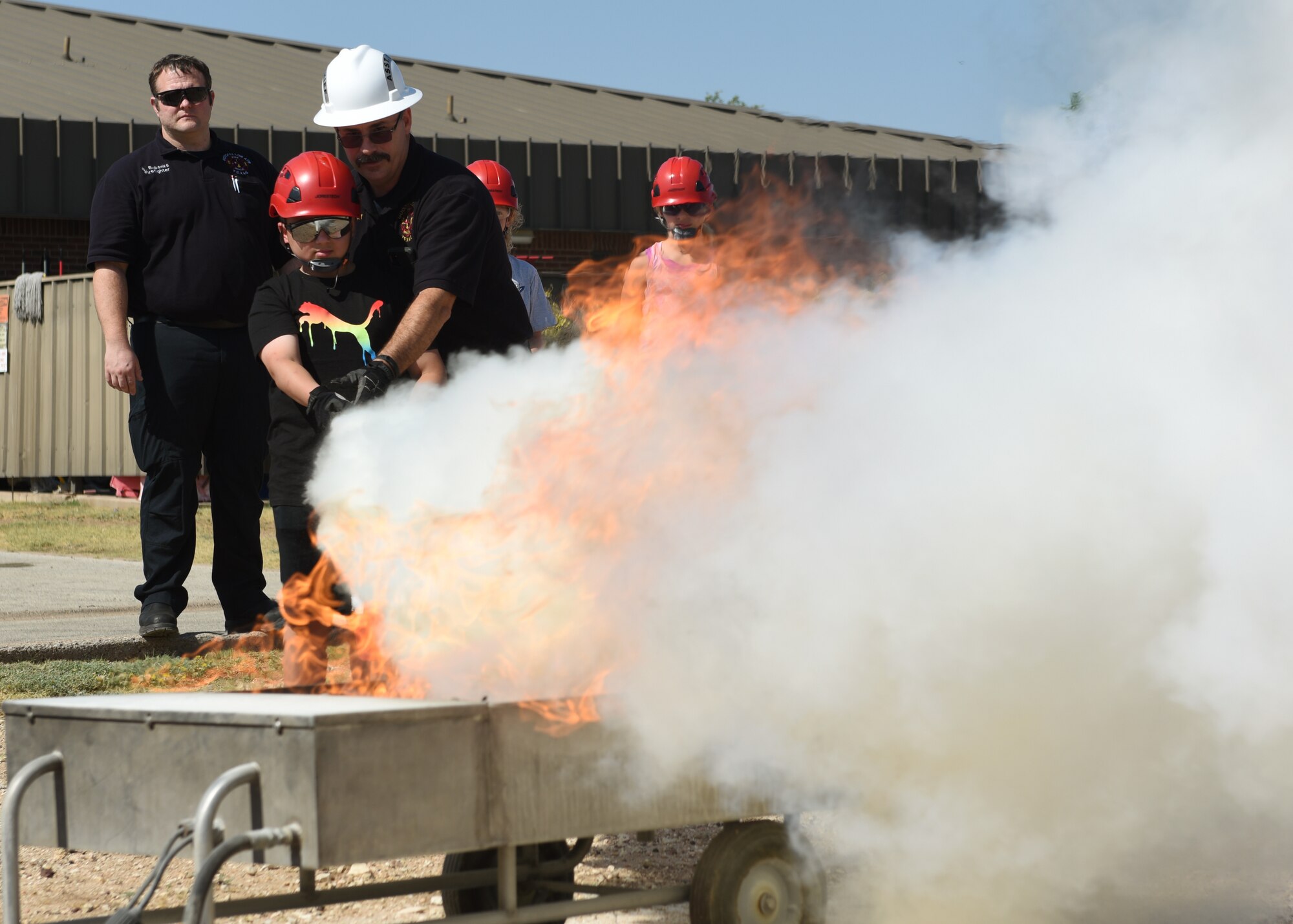 Billy Clemons, 17th Civil Engineer Squadron assistant chief of prevention, guides Cristian Quintanilla, junior firefighter camp student, to extinguish a controlled class-B fire, at Goodfellow Air Force Base, Texas, July 13, 2022. Class B fire extinguishers contain carbon dioxide, which removes oxygen from the fire and suffocates the flames. (U.S. Air Force photo by Airman 1st Class Zachary Heimbuch)