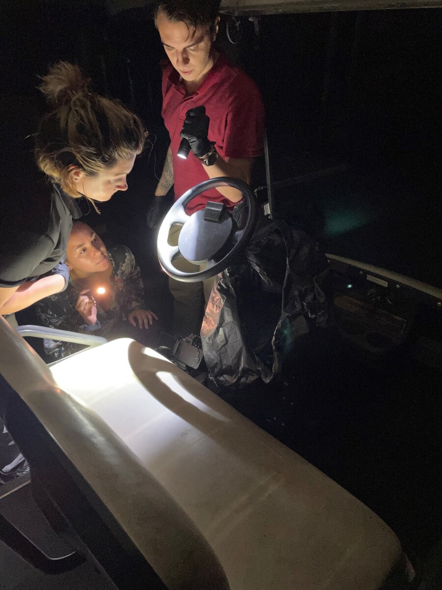U.S. Air Force Special Agent Michelle Jones, 2nd Field Investigations Squadron, Joint Base Andrews, Maryland, left, along with Special Agents Angela Velazquez-Colon, center, and Kenneth Reed, right, Department of the Air Force Office of Special Investigations Detachment 223, use an alternate light source to identify fingerprints on a steering wheel at Tyndall Air Force Base, Florida.