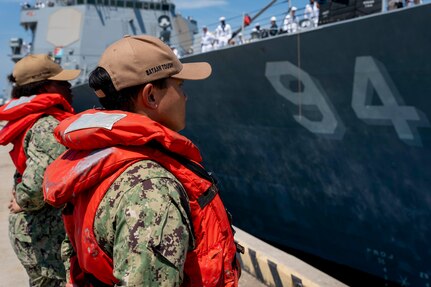 Fireman Wai Yan Han, right, and Retail Specialist Seaman Britany Cooper, assigned to the Wasp-class amphibious assault ship USS Bataan (LHD 5), stand at parade rest as the Arleigh Burke-class guided-missile destroyer USS Nitze (DDG 94) pulls away from the pier to deploy from Naval Station Norfolk, July 17.