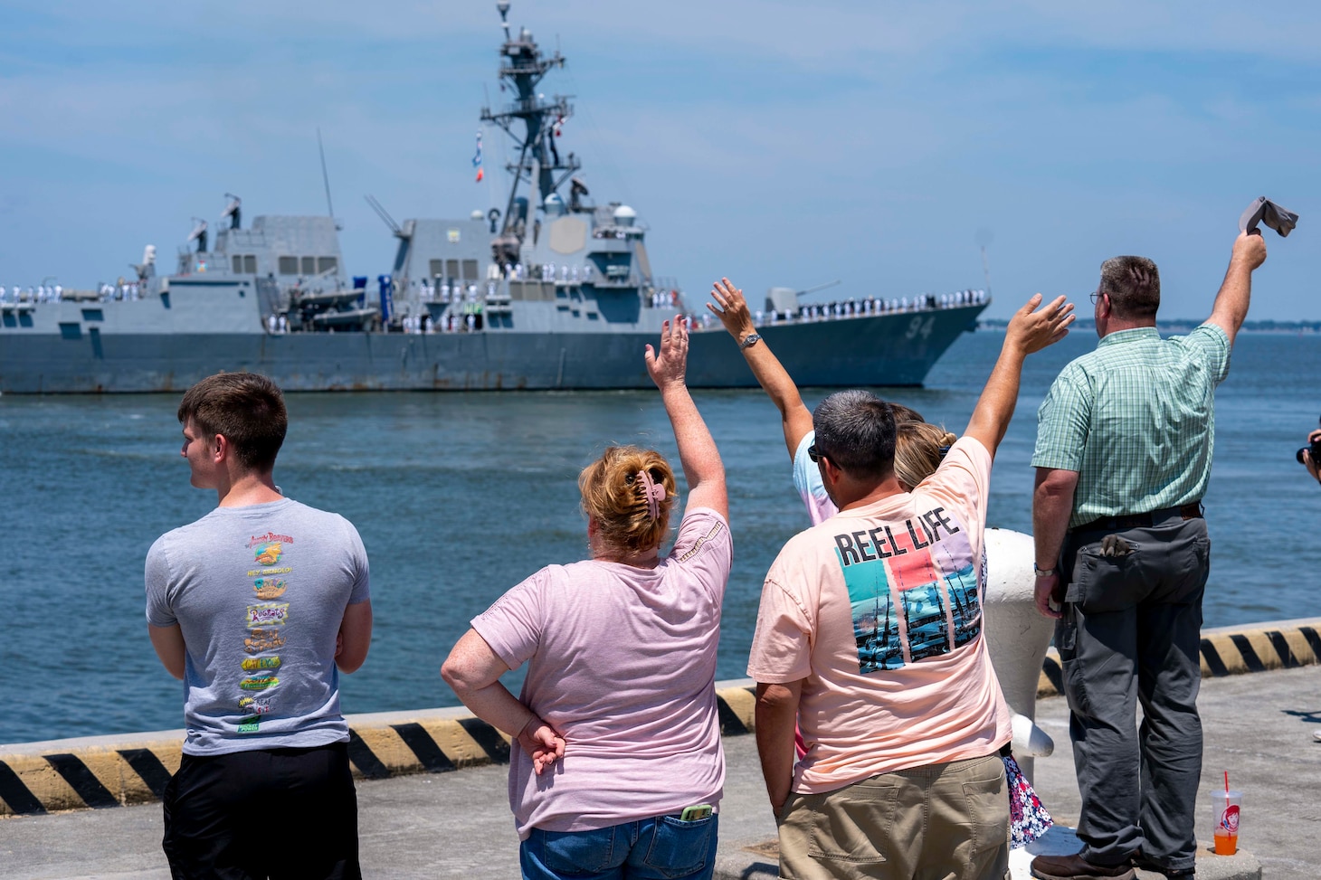Family members wave goodbye to their Sailors as the Arleigh Burke-class guided-missile destroyer USS Nitze (DDG 94) deploys from Naval Station Norfolk, July 17