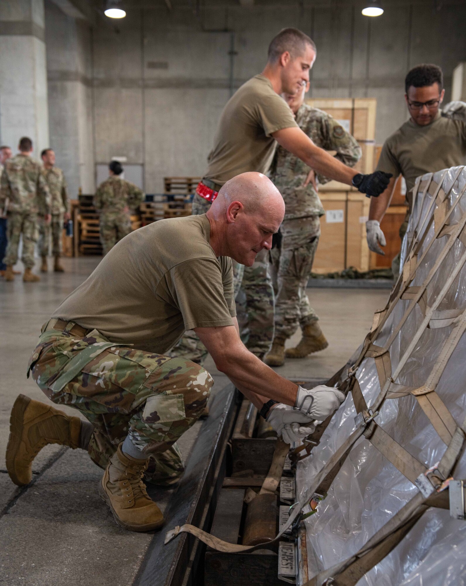 A Colonel helps a bunch of Airmen strap down a pallet