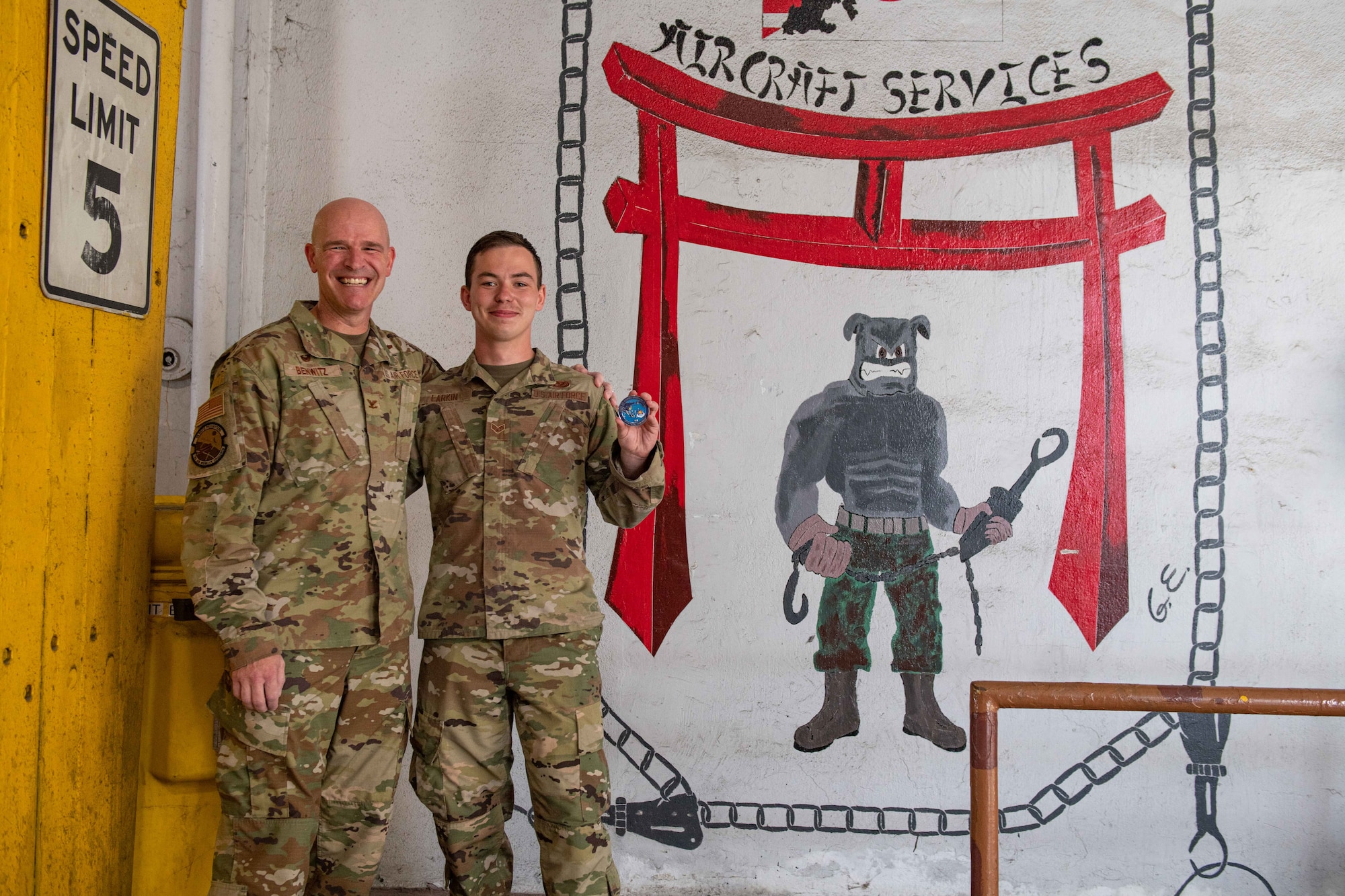 An Airman poses with a Colonel holding a coin