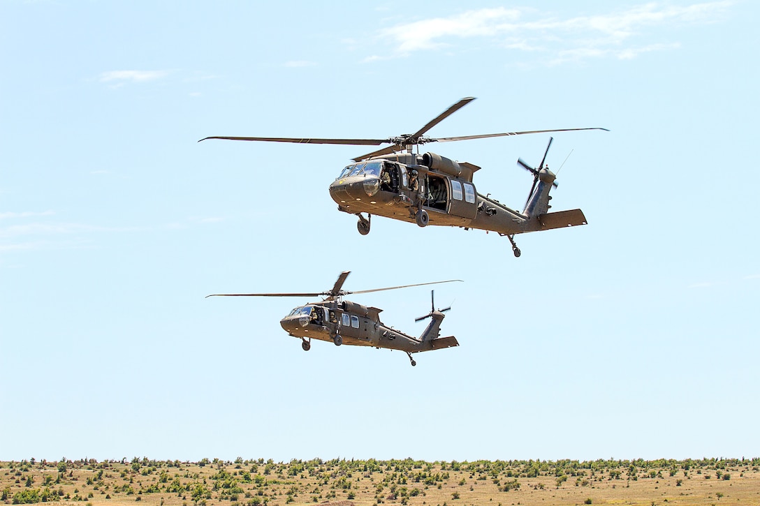 Two helicopters fly above a sparse landscape.