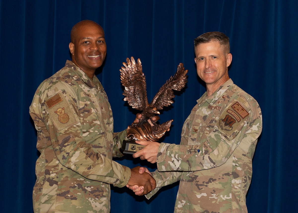 Two men pose for photograph, holding trophy of an eagle in between them
