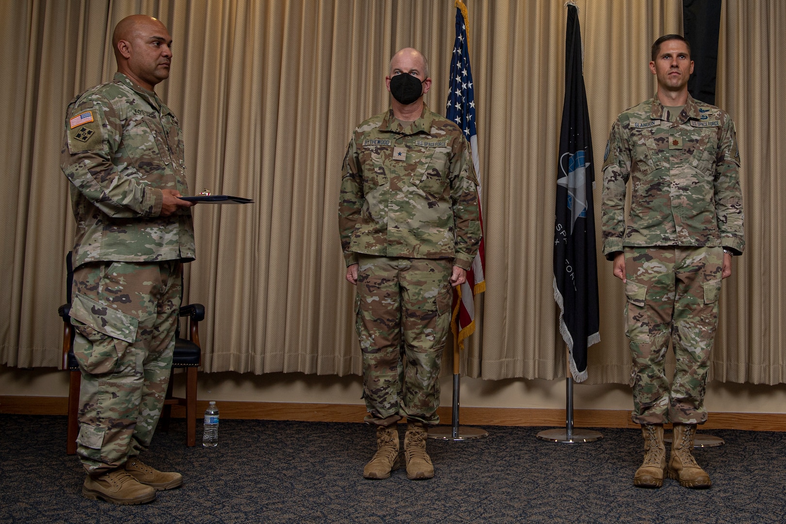 Three military members in uniform stand at attention prior to an award presentation