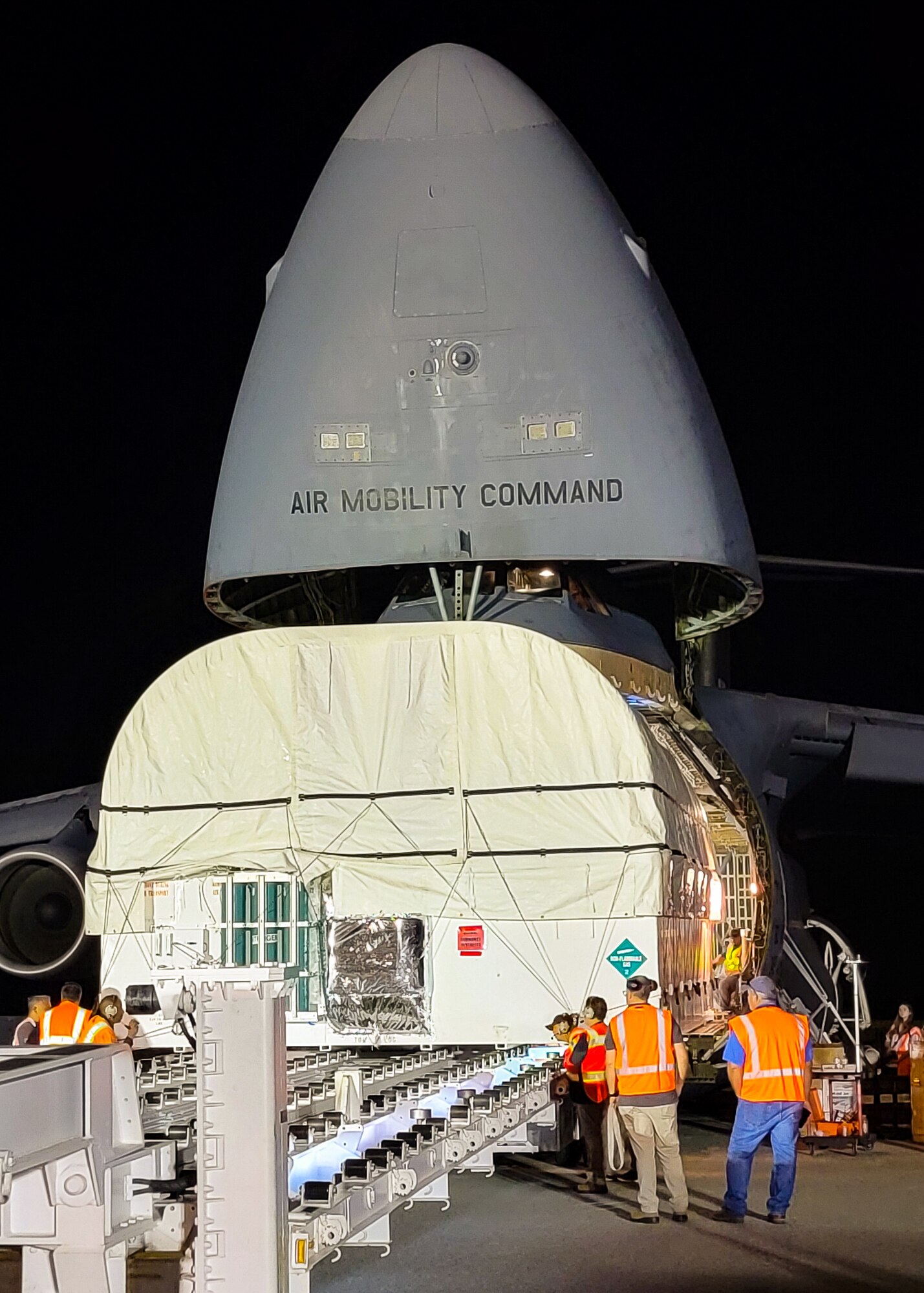 A large military aircraft is being loaded by a large white container.