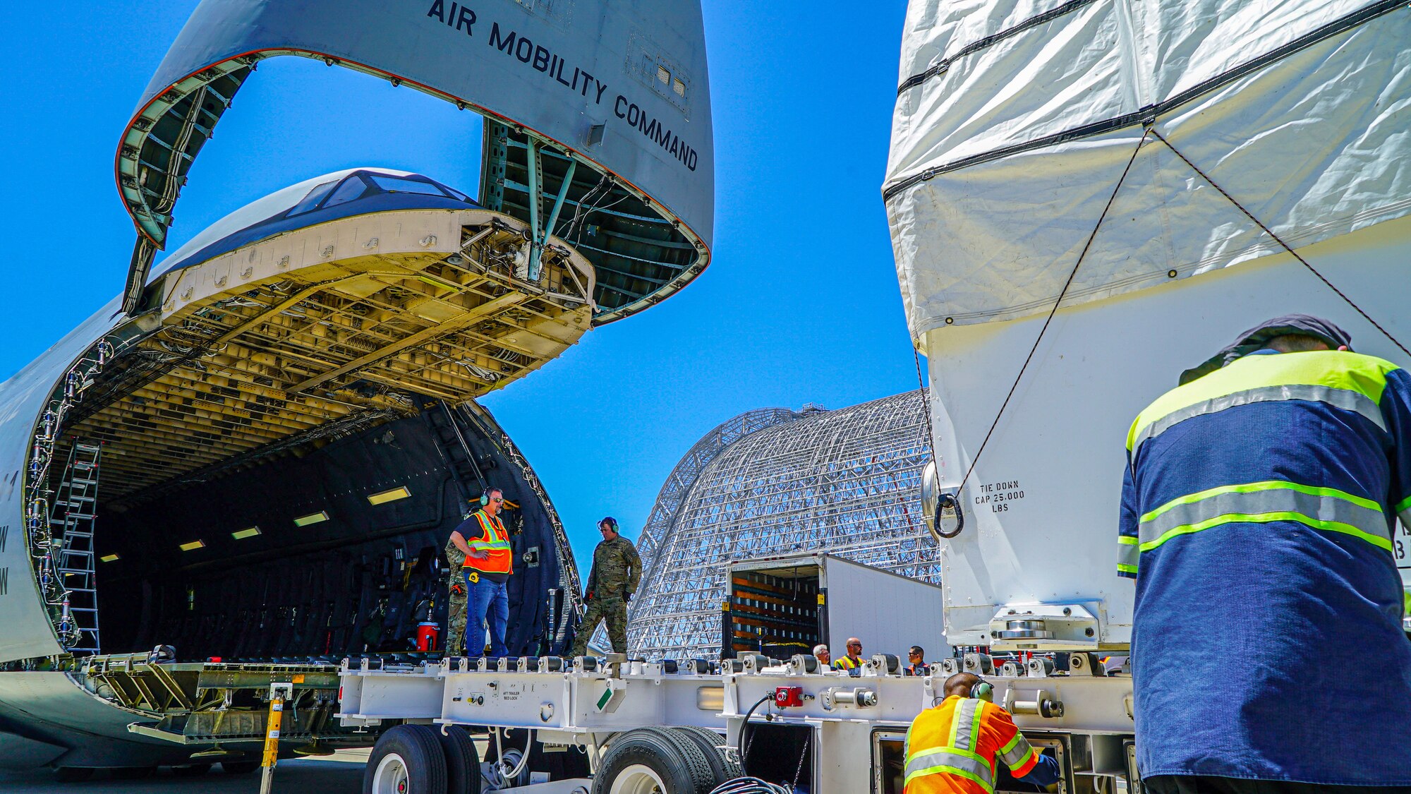 A large military aircraft is being loaded with a large white container.