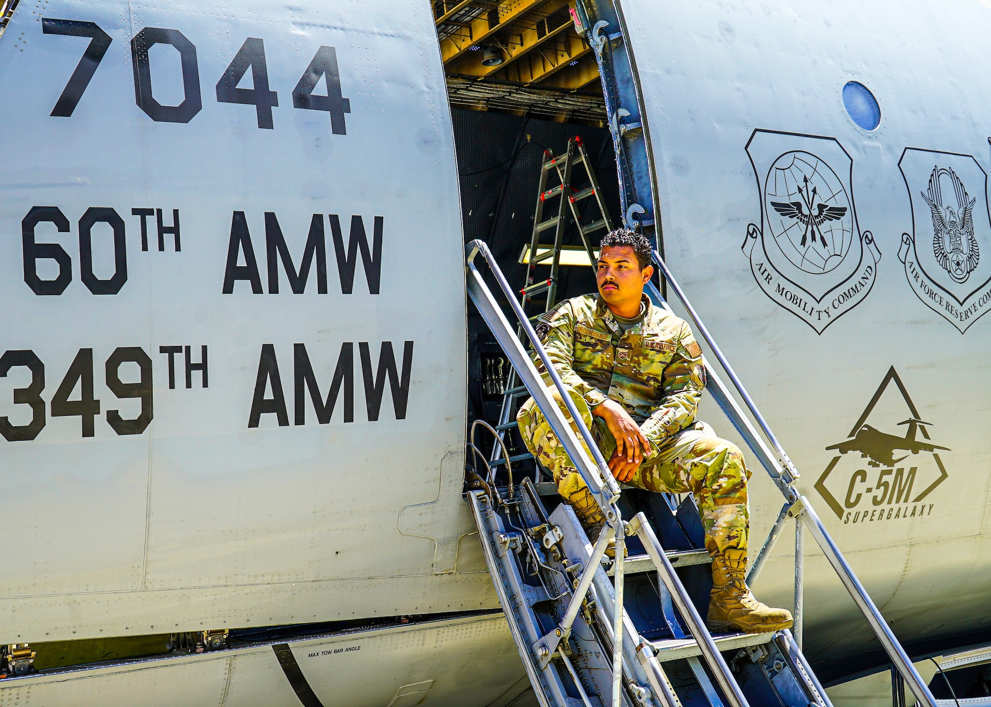 An Airman is sitting down on the ladder used to climb into the plane.