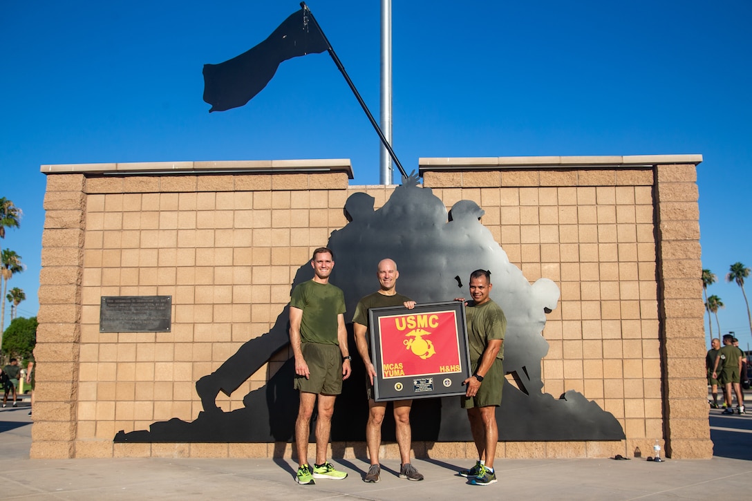 U.S. Marine Corps Lt. Col. Robert Reinoehl, center, commanding officer, Maj. Joshua Woods, left, executive officer, and Sgt. Maj. Hector Hernandez, sergeant major, Headquarters and Headquarters Squadron, pose for a photo with Reinoehl’s farewell gift after a squadron physical training event at Marine Corps Air Station Yuma, Arizona, June 29, 2022.