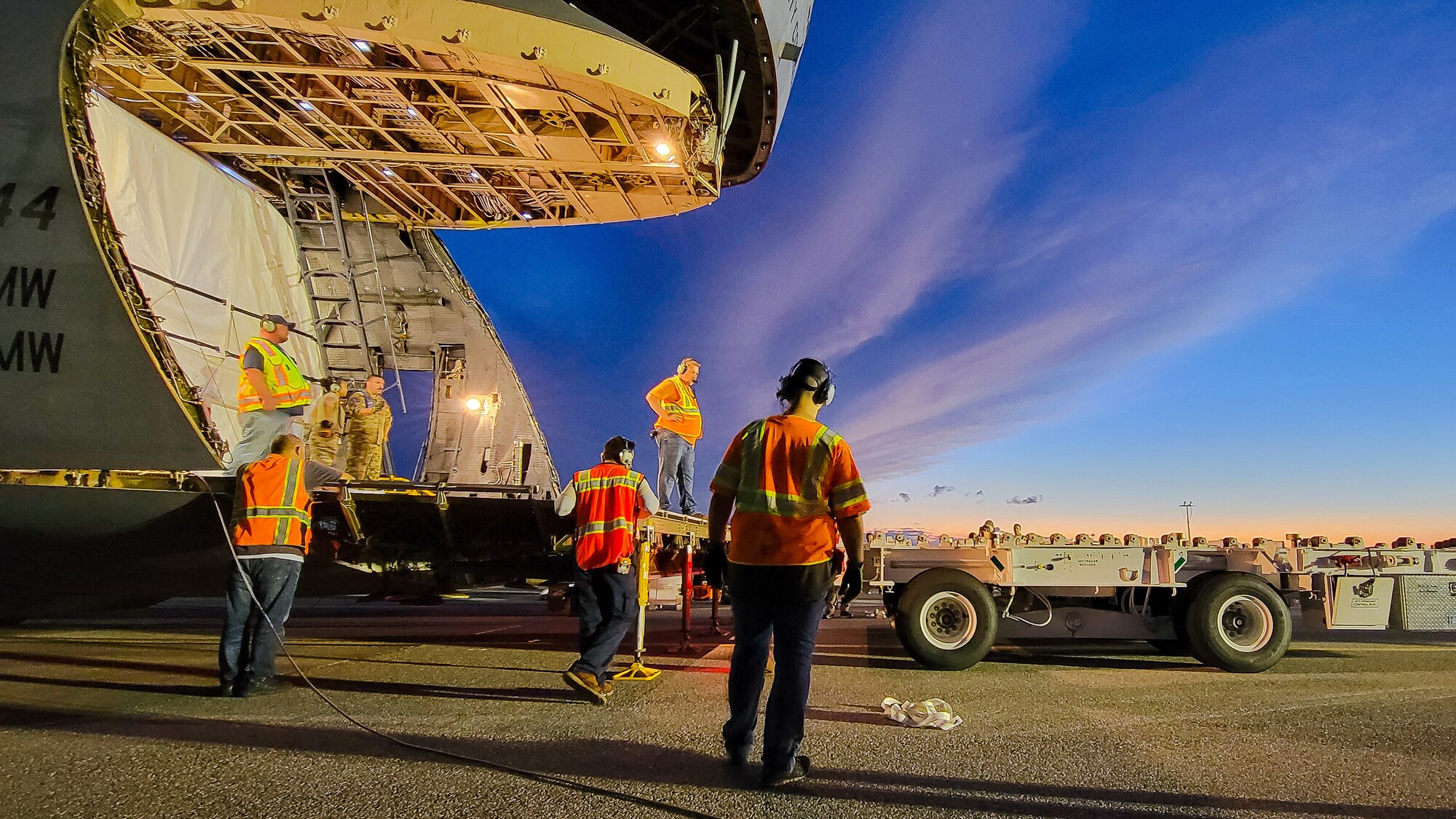 A large military aircraft is being loaded by a large white container.