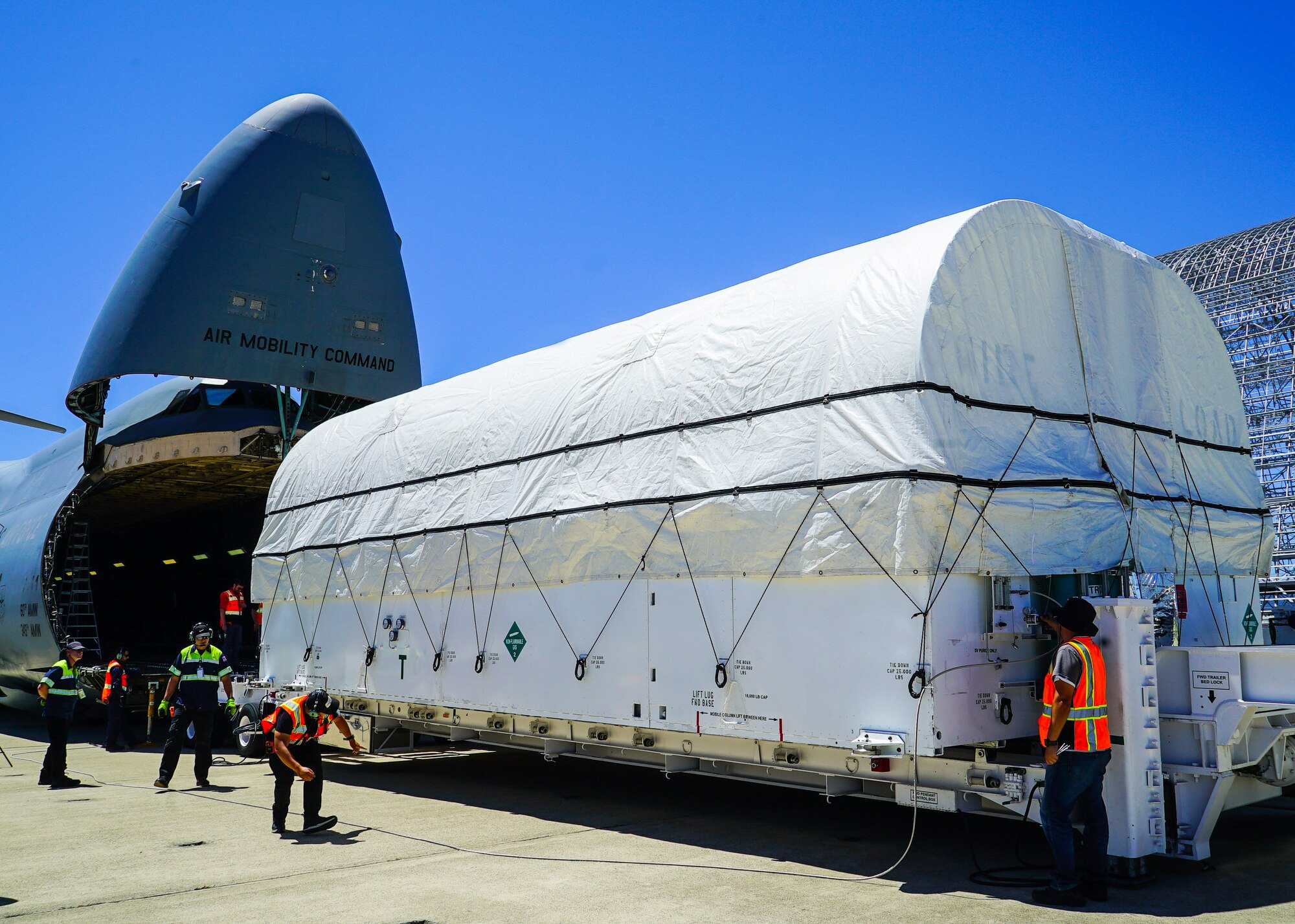 A large military air plane is being loaded with a large white container.