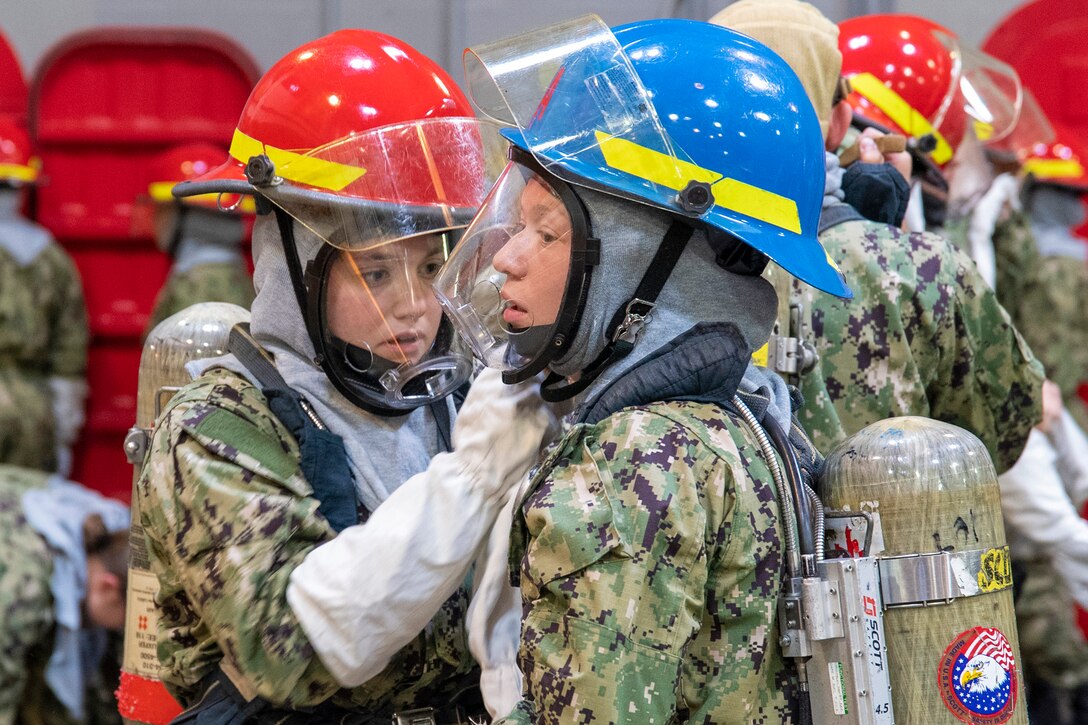 A student helps another put on helmet equipment.