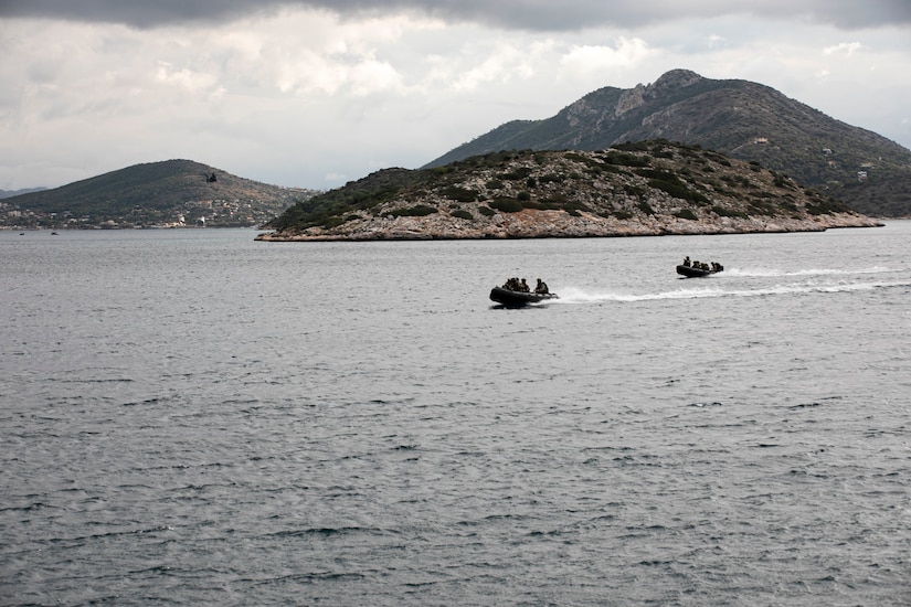 Two small boats chase each over a body of water. Mountains are in the background.