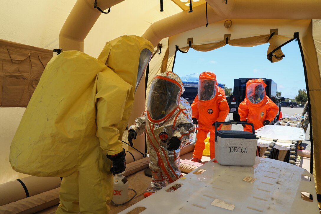 A group of service members wearing hazmat suits enter a tent.