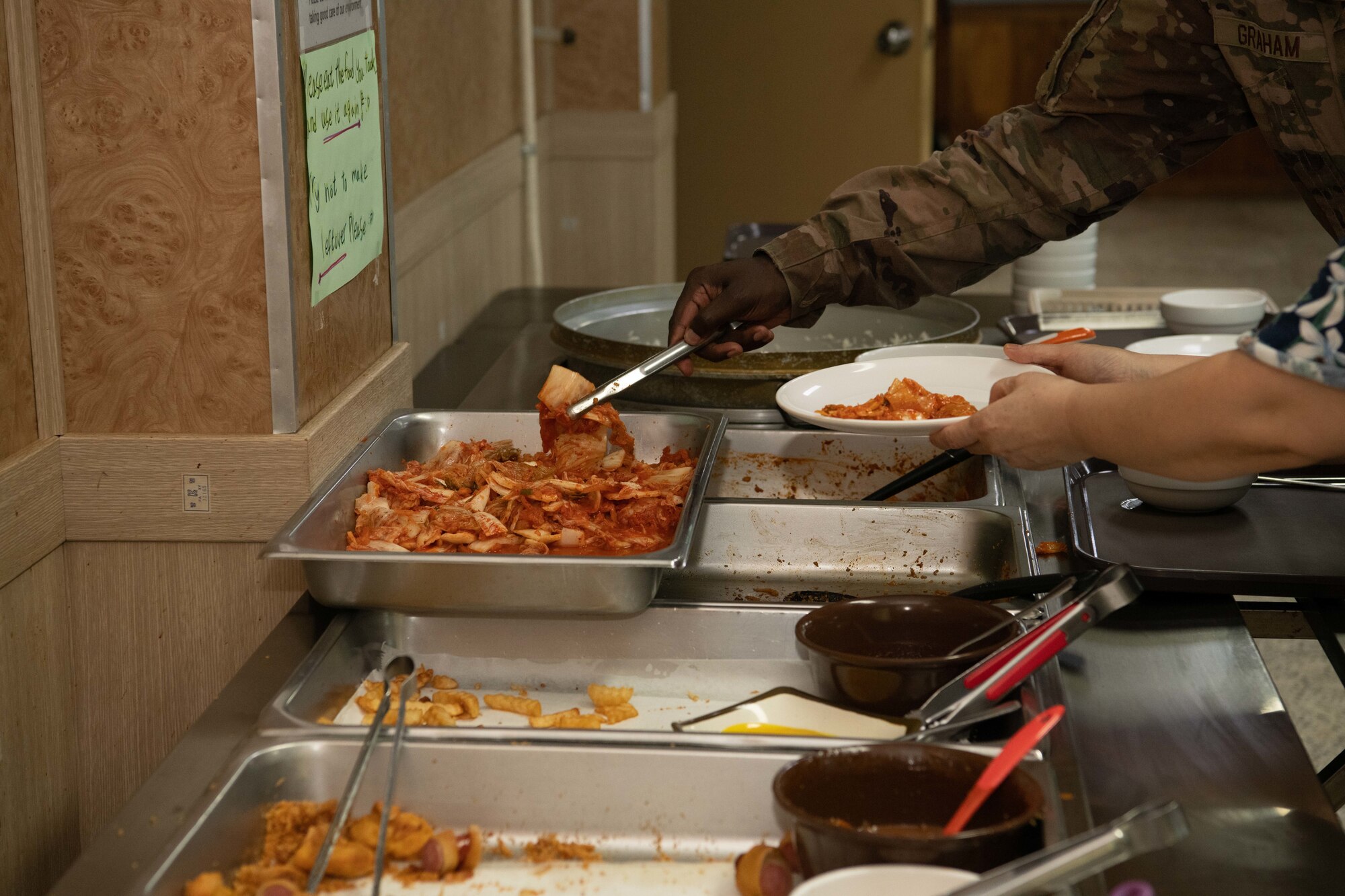A U.S. Air Force service member grabs some kimchi made at Gun Sung Maru at Kunsan Air Base, Republic of Korea, July 8, 2022. Gun Sung Maru was operational for five years on the installation, feeding and introducing Korean cuisine to many Wolf Pack service members. (U.S. Air Force photo by Staff. Sgt. Sadie Colbert)