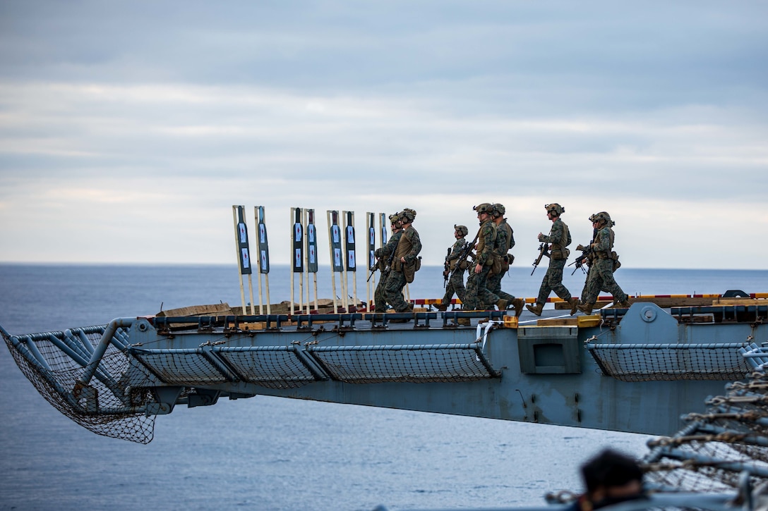 Marines run toward shooting targets on a ship.