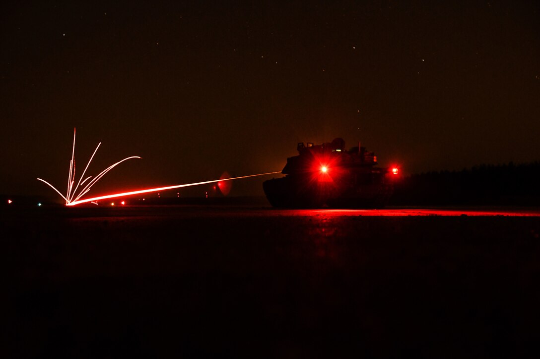 Weapons fire from a tank creates bursts of light against the night sky.