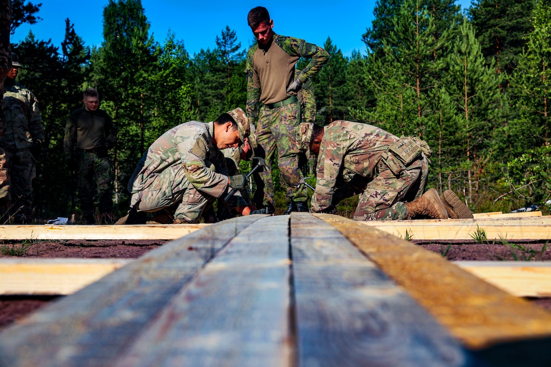 Soldiers hammer nails into a wooden structure.