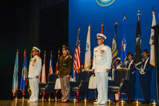 Military personnel stand at attention on a stage.
