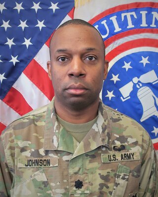 man in u.s. army uniform standing in front of two flags.