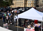 People stand in line for food in a parking lot.