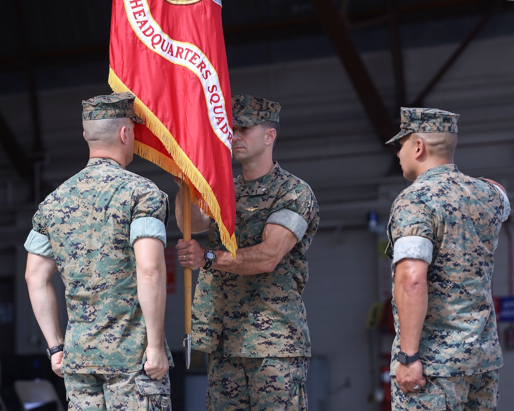 U.S. Marine Corps Lt. Col. Michael Hayes, center, oncoming commanding officer, Headquarters and Headquarters Squadron (H&HS), Marine Corps Air Station (MCAS) Yuma, Arizona, receives the unit colors from Lt. Col. Robert Reinoehl, left, outgoing H&HS commanding officer, during a change of command ceremony aboard the installation, June 30, 2022. Reinoehl commanded H&HS for two years and relinquished command to Hayes, previously the MCAS Yuma operations officer. (U.S. Marine Corps photo by Lance Cpl. Jade Venegas